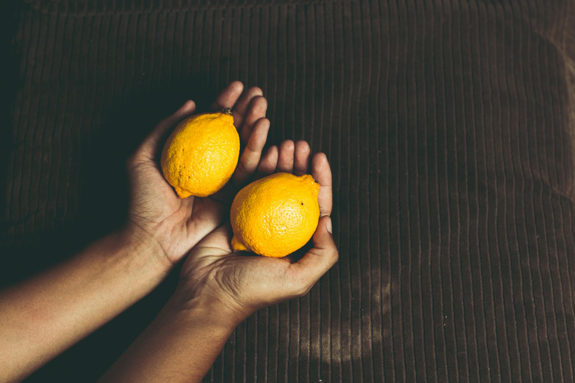 Two fresh lemons held in cupped hands, symbolizing gentle self-care and reconnection.
