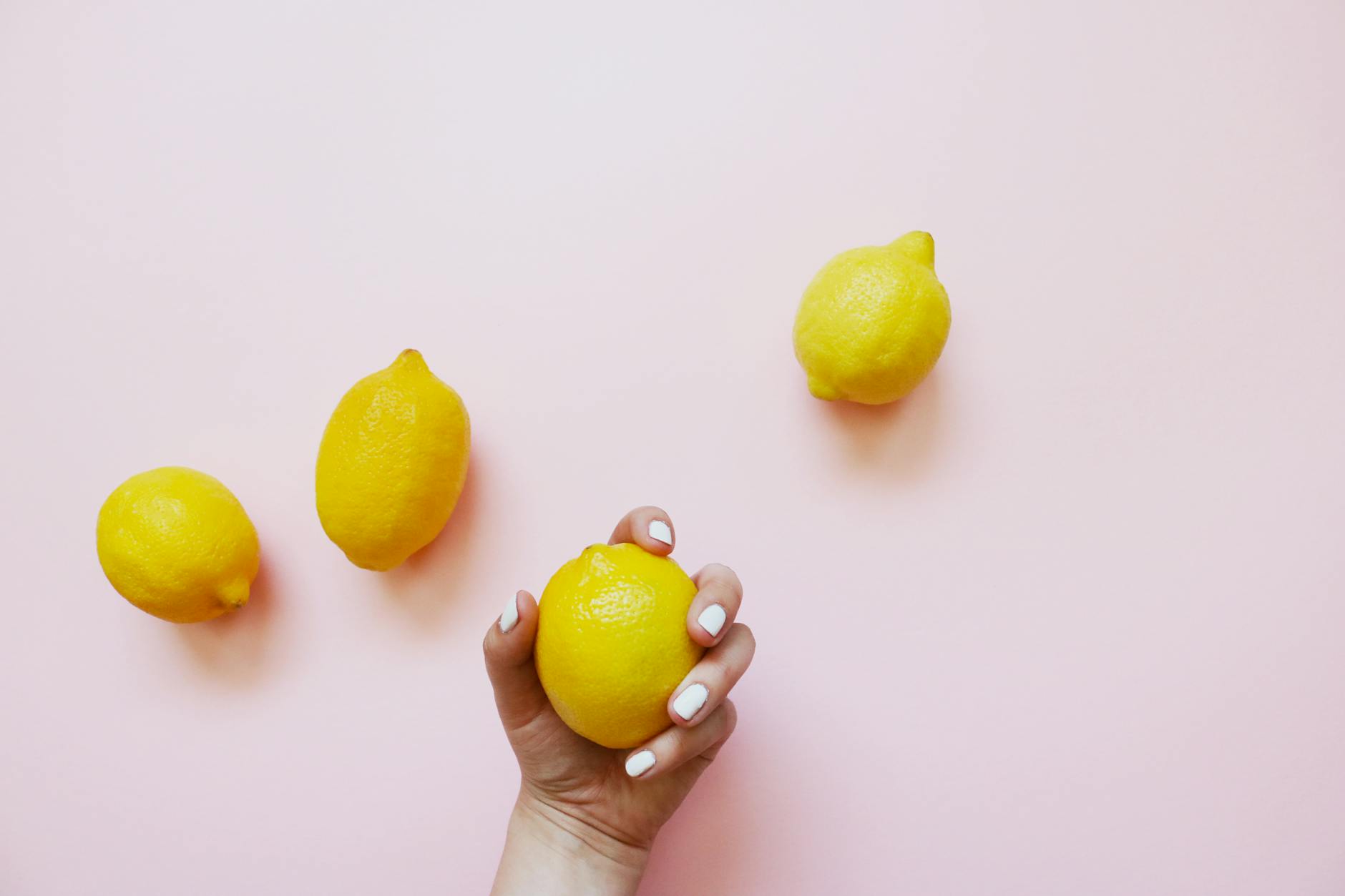 A hand holding a lemon on soft pink background