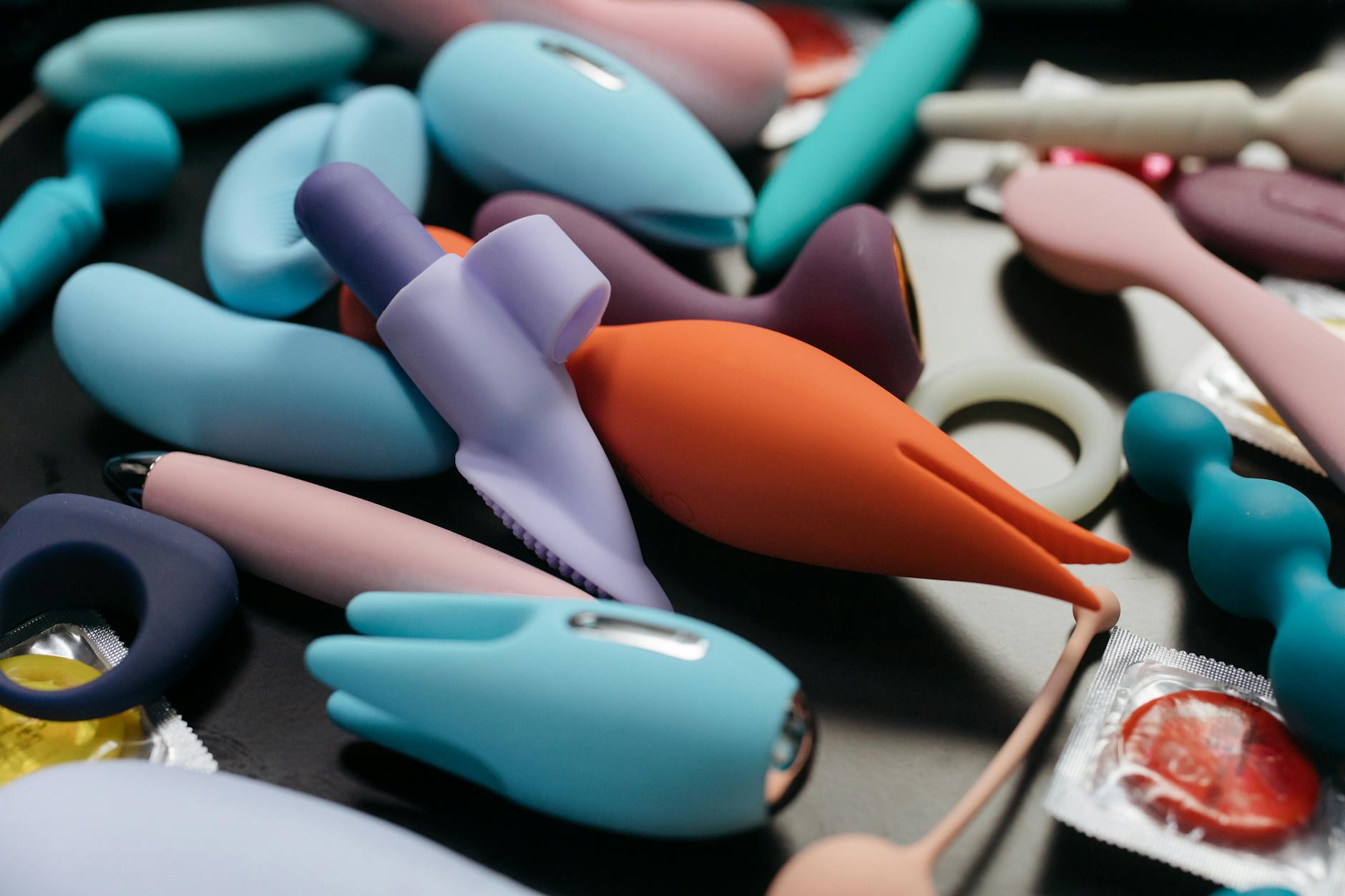 A hand reaching toward colorful vibrators and adult toys arranged on a table.