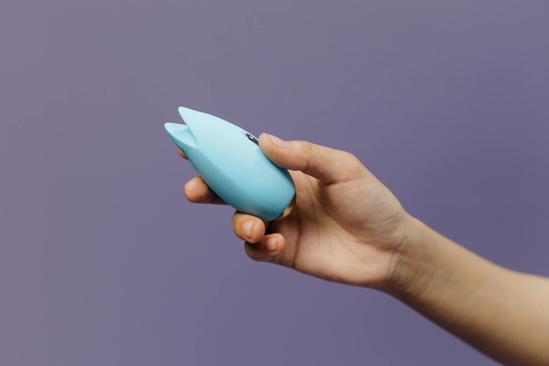 A hand holding a blue lemon clitoral vibrator against a purple background