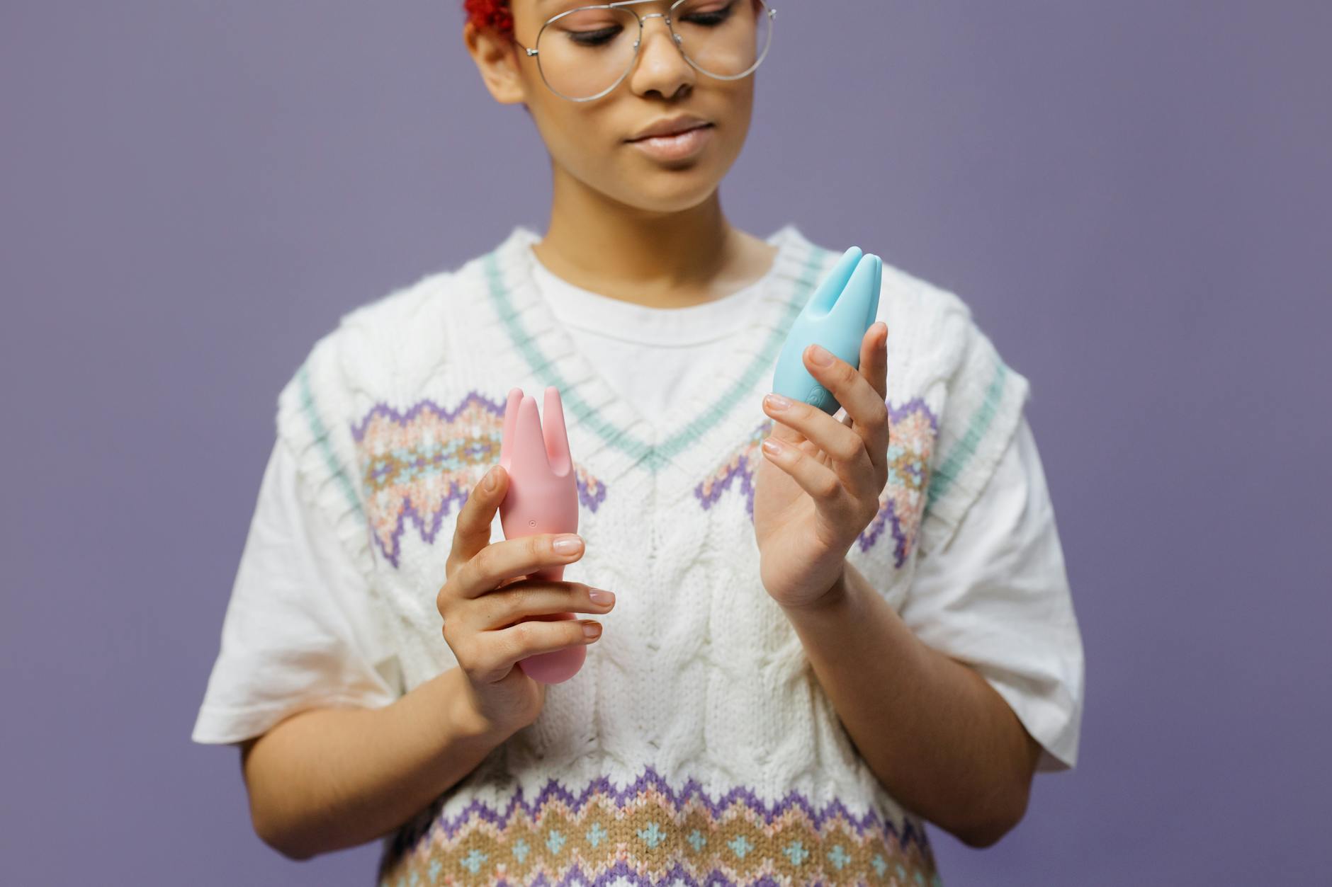 Woman holding blue and pink silicone vibrators in a thoughtful, empowered moment.