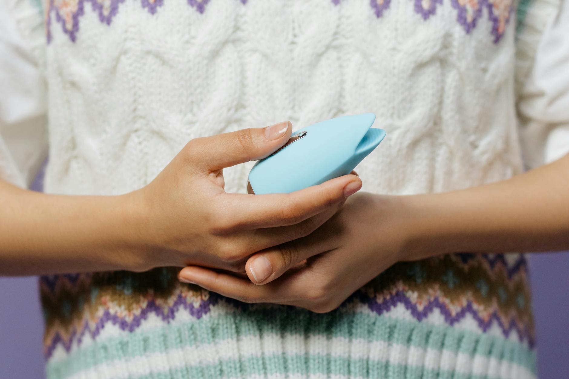 Close-up of hands holding a blue vibrator against knitted fabric, showing intimate self-care